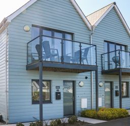 A two-story house with blue siding and glass balconies with chairs at Seaquel in Westward Ho