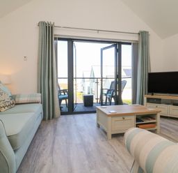 A living room with sofas a coffee table a tv and glass doors leading to a balcony at Seaquel in Westward Ho