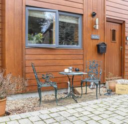A small metal table with two metal chairs outside a wood-paneled house with a door and window at Maple in Falmouth