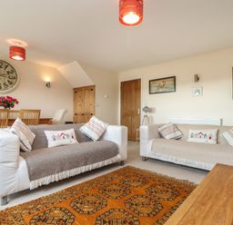 A living room with two sofas a wooden dining table with chairs a large wall clock and wall art at Maple in Falmouth