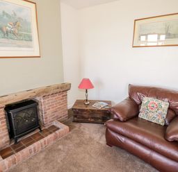 A room with a leather armchair and a brick fireplace with a wood stove at Manor Farm Cottage in Hill Croome near Upton Upon Severn