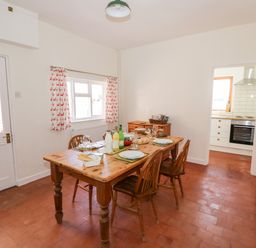 A dining room with a wooden table set for four and a view into a kitchen at Manor Farm Cottage in Hill Croome near Upton Upon Severn
