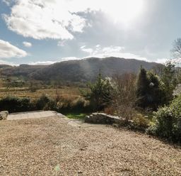 A gravel driveway with bushes and trees and hills in the background at The Old Smithy Cottage in Maentwrog near Penrhyndeudraeth