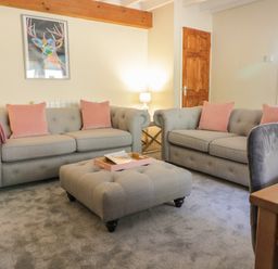 A living room with two grey sofas with pink cushions a grey ottoman and a wooden door at The Old Smithy Cottage Maentwrog near Penrhyndeudraeth