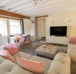 A living room with a TV on a white stand a dining table with chairs and couches with pink cushions at The Old Smithy Cottage in Maentwrog near Penrhyndeudraeth
