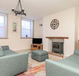 A living room with two teal sofas a gray stove in a fireplace a round clock on the wall a wooden cabinet and a colorful rug at Bliss On The Bay in Weymouth