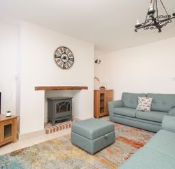 A living room with teal sofas a wooden TV stand a wall clock and a fireplace at Bliss On The Bay in Weymouth
