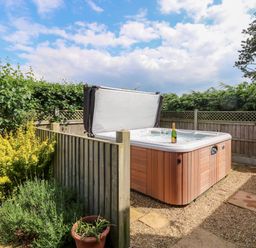 An outdoor hot tub partially surrounded by wooden fencing with plants and greenery around at Spinney's Den in Knapton