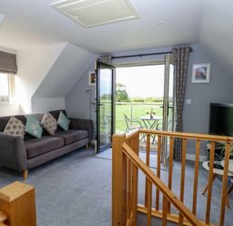 A sitting area with a sofa and cushions a small table with plant a television and doors opening to a patio at Spinney's Den in Knapton