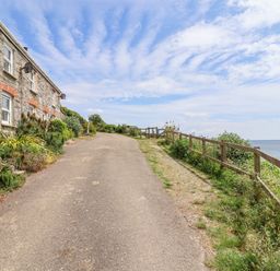 A pathway beside a stone house leading to the ocean at 2 Cliff Cottages West Portholland near Gorran Haven