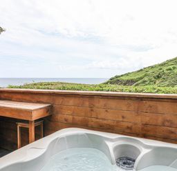 An outdoor area with a hot tub and wooden seating overlooking the ocean at 2 Cliff Cottages West Portholland near Gorran Haven