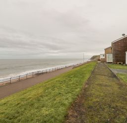 A seaside walkway with railings next to houses and a grassy area at Sea Snug in Spittal