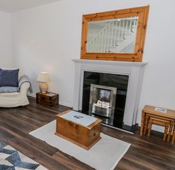 A living room with an armchair a lamp wooden tables fireplace and a mirror at 22 Gwel Yr Wyddfa in Menai Bridge