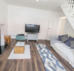 A living room with a sofa under stairs a television on a stand and a fireplace at 22 Gwel Yr Wyddfa in Menai Bridge