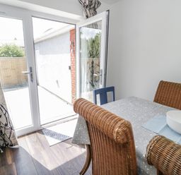 A dining area with wicker chairs around a table covered with a tablecloth and a white bowl near glass doors leading outside at 22 Gwel Yr Wyddfa in Menai Bridge