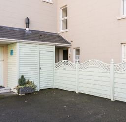 An exterior area with a light green door and storage shed next to a cream building and three light green wooden fences
