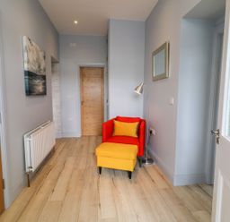 A hallway with a red chair and yellow ottoman next to a floor lamp and mirror at Beachcomber Ballycastle