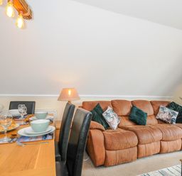 A dining table set with plates glasses and a bottle next to a brown sofa with cushions in a living room at Dart Lodge in Callington