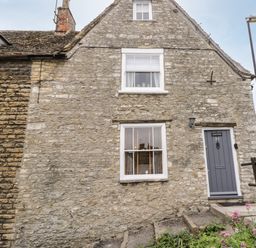 Stone exterior of a house with two windows and a gray door at Corner Cottage in Malmesbury