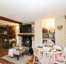 A dining area with a round table set for four next to a fireplace with a TV above at Corner Cottage in Malmesbury