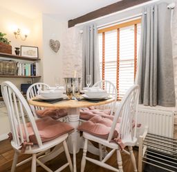 A dining area with a round wooden table and four white chairs with pink cushions at Corner Cottage in Malmesbury