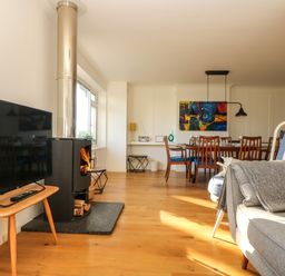 A living room with a wood stove television dining table and chairs at Rock Pool House in Porthleven