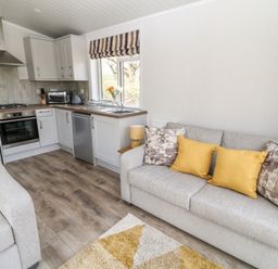 A kitchen and living area with gray sofas yellow and patterned cushions and wooden floor at Dove Lodge in Highampton near Sheepwash