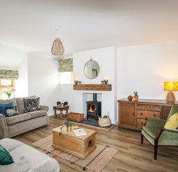 A living room with two sofas a green armchair wooden chest coffee table wood stove and wooden sideboard at Plas Coch Rhoscolyn in Rhoscolyn