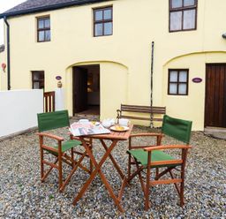 An outdoor seating area with two chairs and a table set with breakfast items in front of a yellow building at The Stable in Fethard-On-Sea County Wexford