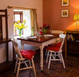 A dining area with a wooden table set for two and white chairs with red cushions at The Stable in Fethard-On-Sea County Wexford