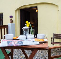 An outdoor wooden table with cups plates pastries a newspaper a French press and a yellow flower in a glass at The Stable in Fethard-On-Sea County Wexford