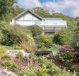 A modern house with a glass balcony surrounded by a garden with various plants and flowers at Kessock in Bowness-On-Windermere