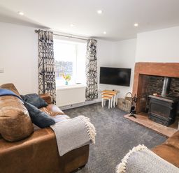 A living room with leather sofas curtains a window a wall mounted tv and a fireplace at Sparrow Cottage in Keswick