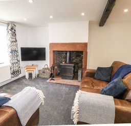 A living room with brown leather sofas a fireplace and a wall-mounted TV at Sparrow Cottage in Keswick