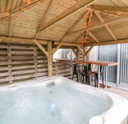 An outdoor covered area with a hot tub a bar table and chairs at Fistral Apres Surf in Newquay