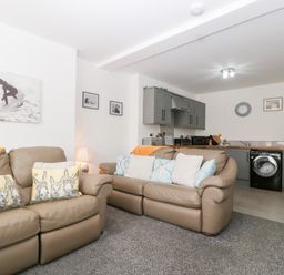 A living room with couches and a kitchen area at 76A Mackworth Road in Porthcawl