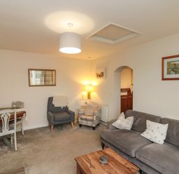 A living room with a gray sofa a wooden coffee table two armchairs a dining table with chairs and framed pictures on the walls at Chestnut Cottage in Filey