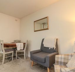 A room with a wooden dining table and three chairs a gray armchair with a blanket and a plaid armchair at Chestnut Cottage in Filey