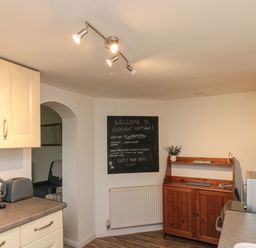 A kitchen with cream cabinets a wooden sideboard a microwave and a chalkboard with welcome message at Chestnut Cottage in Filey