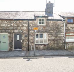 Stone cottage with three doors and three windows on a paved sidewalk at Weaver's Cottage in Tremadog