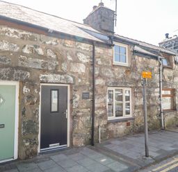 Stone exterior of a row of cottages with doors and windows on a street with a sign at Weavers Cottage in Tremadog