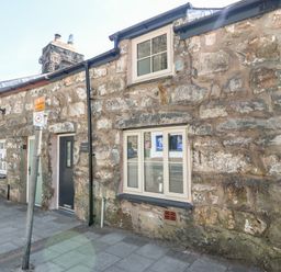 A stone cottage with two windows and two doors beside a sidewalk with a street sign at Weavers Cottage in Tremadog