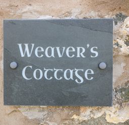 A stone plaque with the text Weavers Cottage mounted on a rough stone wall at Weavers Cottage Tremadog