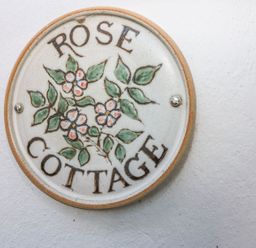 A round ceramic sign with flowers and leaves on a wall at Rose Cottage in Marldon