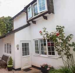 Exterior of a white house with windows a door a bench and flowers at Rose Cottage in Marldon
