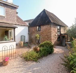 A gravel pathway with plants and a flower pot beside a stone building with a thatched roof at Rose Cottage in Marldon