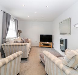 A living room with striped sofas a television on a wooden stand and a wall-mounted fireplace at Fonthill in Torquay