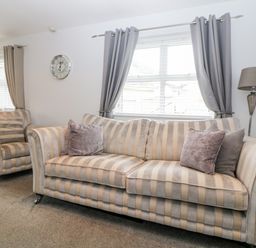A living room with a striped sofa and armchair under windows with gray curtains at Fonthill in Torquay