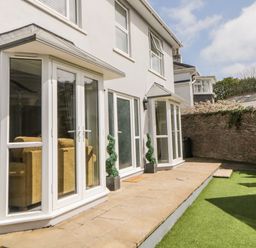 A patio area with stone tiles and artificial grass outside a two-story house with white framed glass doors and windows at Fonthill in Torquay