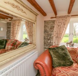 A corner of a room with a patterned sofa cushions window with curtains a radiator and a large ornate mirror on the wall at The Linhay in Holsworthy